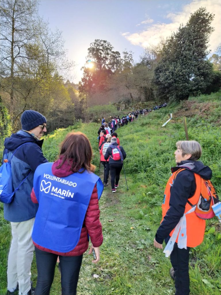 Decenas de senderistas ascienden por un camino por una ladera . En  primer plano tres personas de la organización: dos mujeres y un hombre conversan ante el paso de lsenderistas