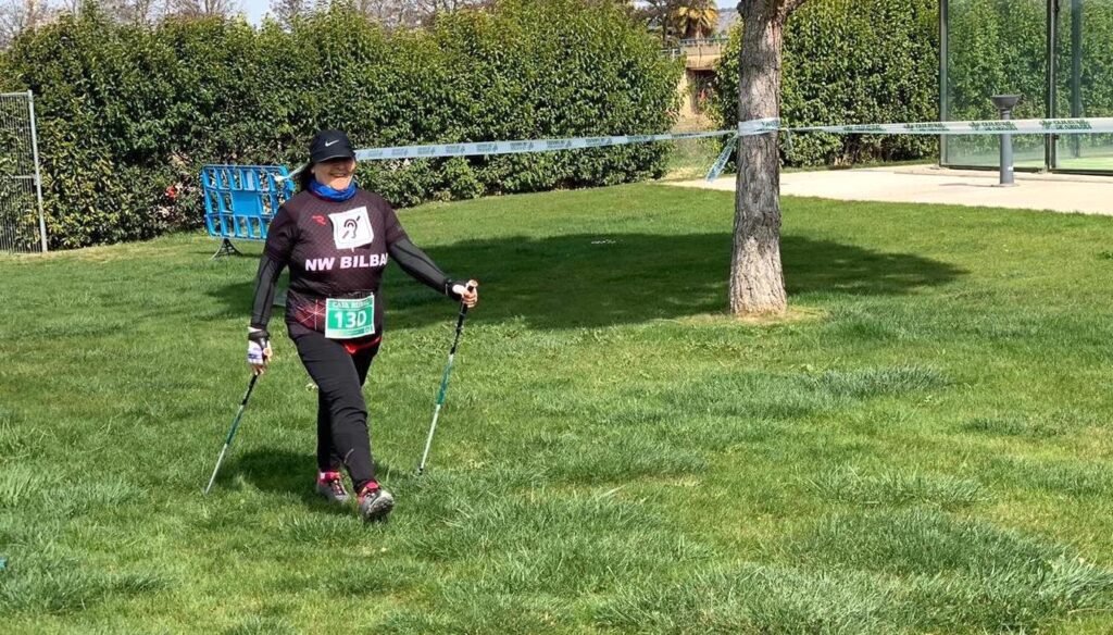 Inma-Sorkunde aparece de cuerpo entero en un momento de la competición, sonriente y con una muy buena técnica de marcha nórdica. Camina sobre hierba. 