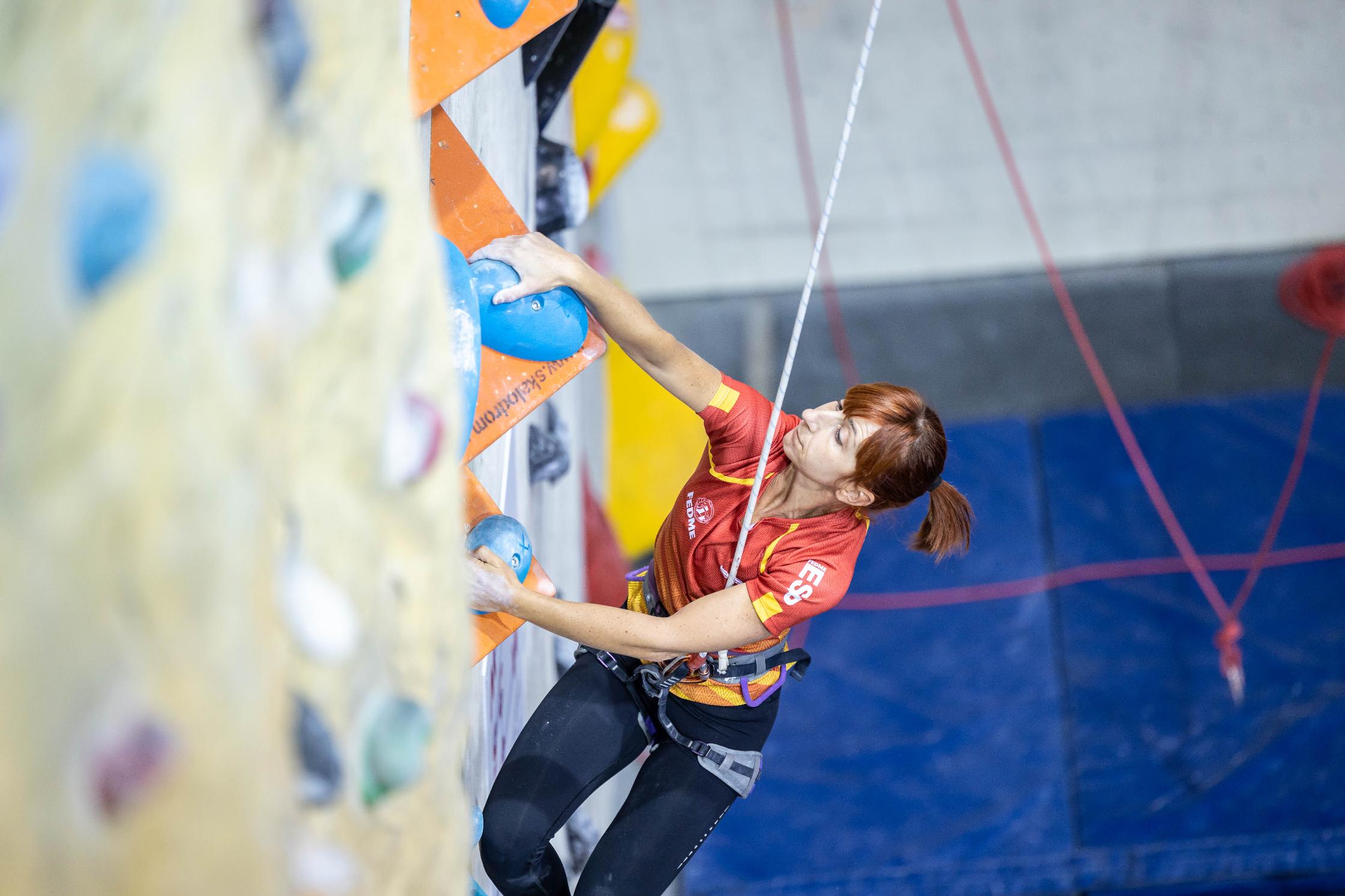 Foto de Portada: Marta está ascendiendo por un rocódromo, en posición lateral, su mirada se fija en su mano derecha que agarra una presa azul