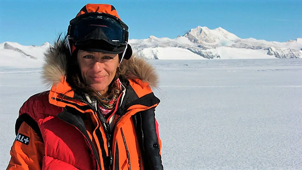 Foto de portada: En primer plano se ve a Chus Lago de cintura para arriba equipada con vestimenta invernal de montaña, anorak con gorro de color naranja. De fondo una planicie helada con montañas nevadas tras ella.