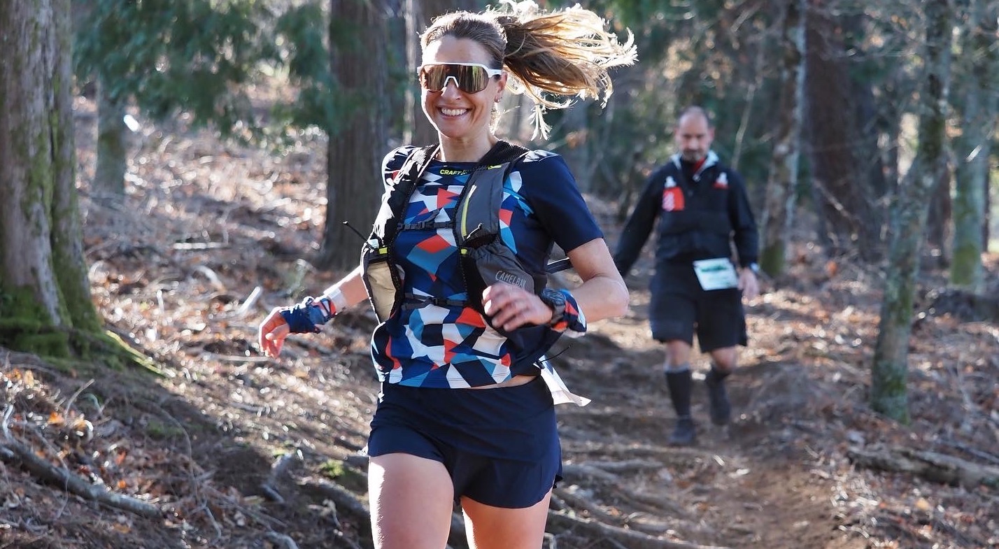 Descripción de la foto de portada: Aroa está corriendo por un bosque en una carrera por montaña. Lleva pantalón corto, chaleco de corredora y gafas de sol. A pesar de ir corriendo luce una amplia sonrisa. A su alrededor se ven los troncos de los árboles del bosque y detrás de ella, por el sendero, a un árbitro de la competición.