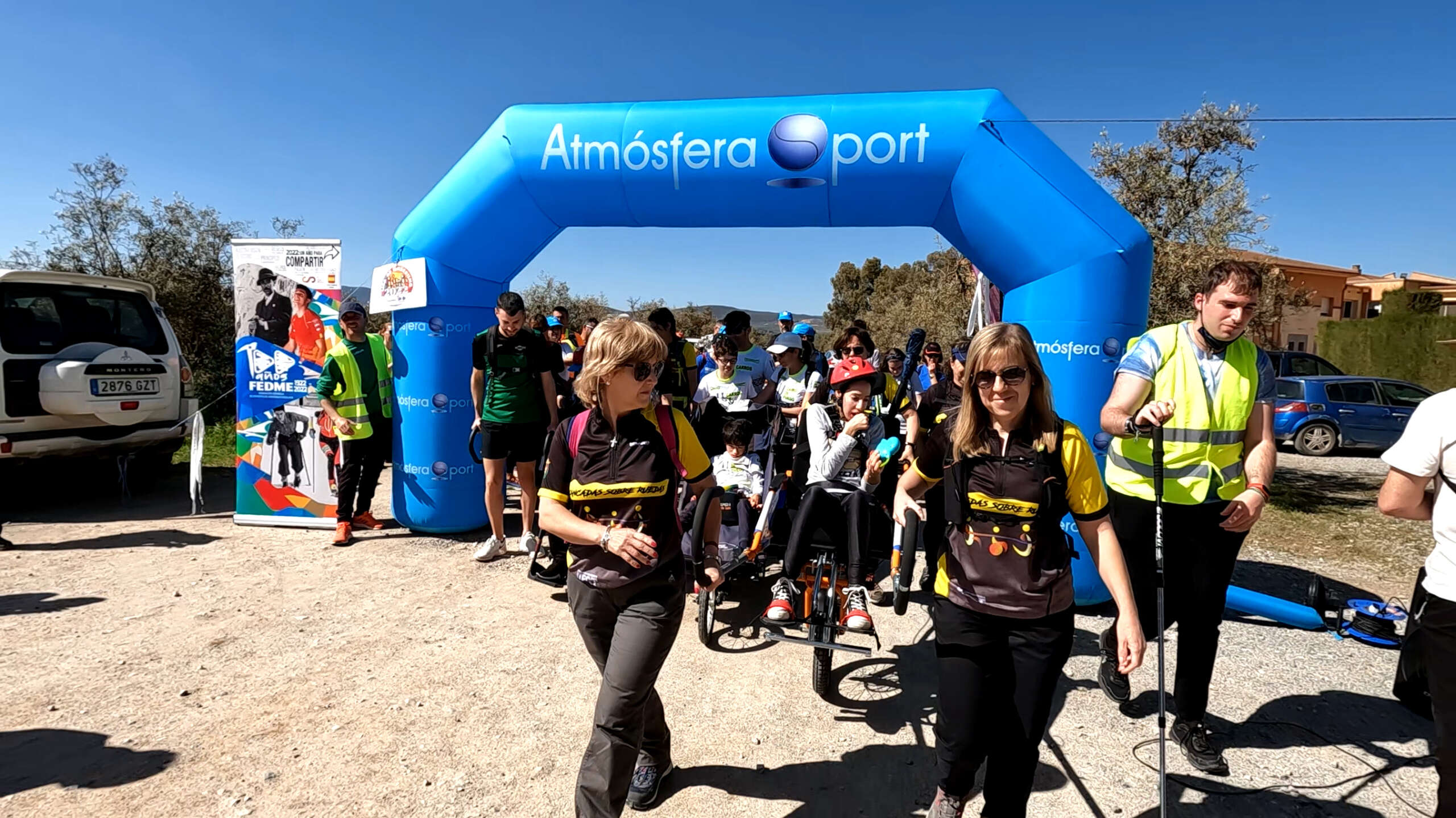 Foto de portada: Foto en color del inicio de la “Ruta Mamut” de la Liga de Senderismo FEDME. Momento del arranque de la actividad donde se visualizan personas en sillas de montaña, acompañadas por las personas de apoyo a la movilización. Al fondo arco de salida con el logo de la Liga de Senderismo y el roll-up del Centenario
