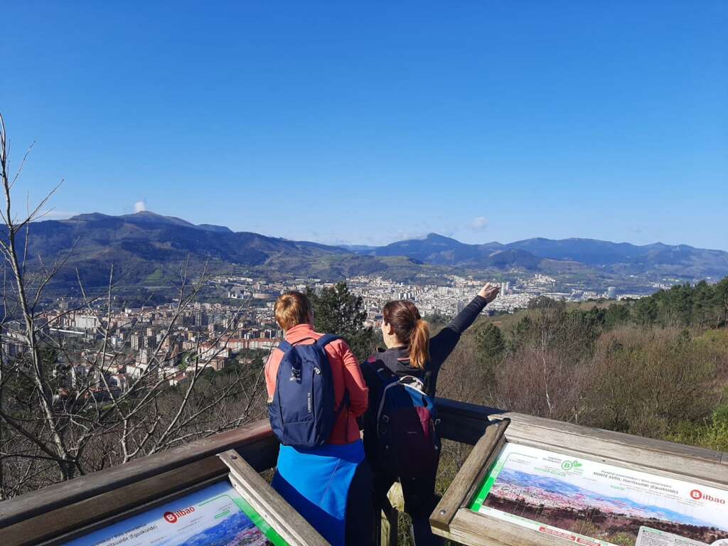 Foto. V Liga de Senderismo de Vizcaya. GR 228. Anillo verde de Bilbao. 13 de marzo. Bilbao
Fotografía que presenta a dos senderistas en un mirador de la ruta, junto a dos mesas interpretativas del paisaje, con la ciudad de Bilbao a sus pies.
