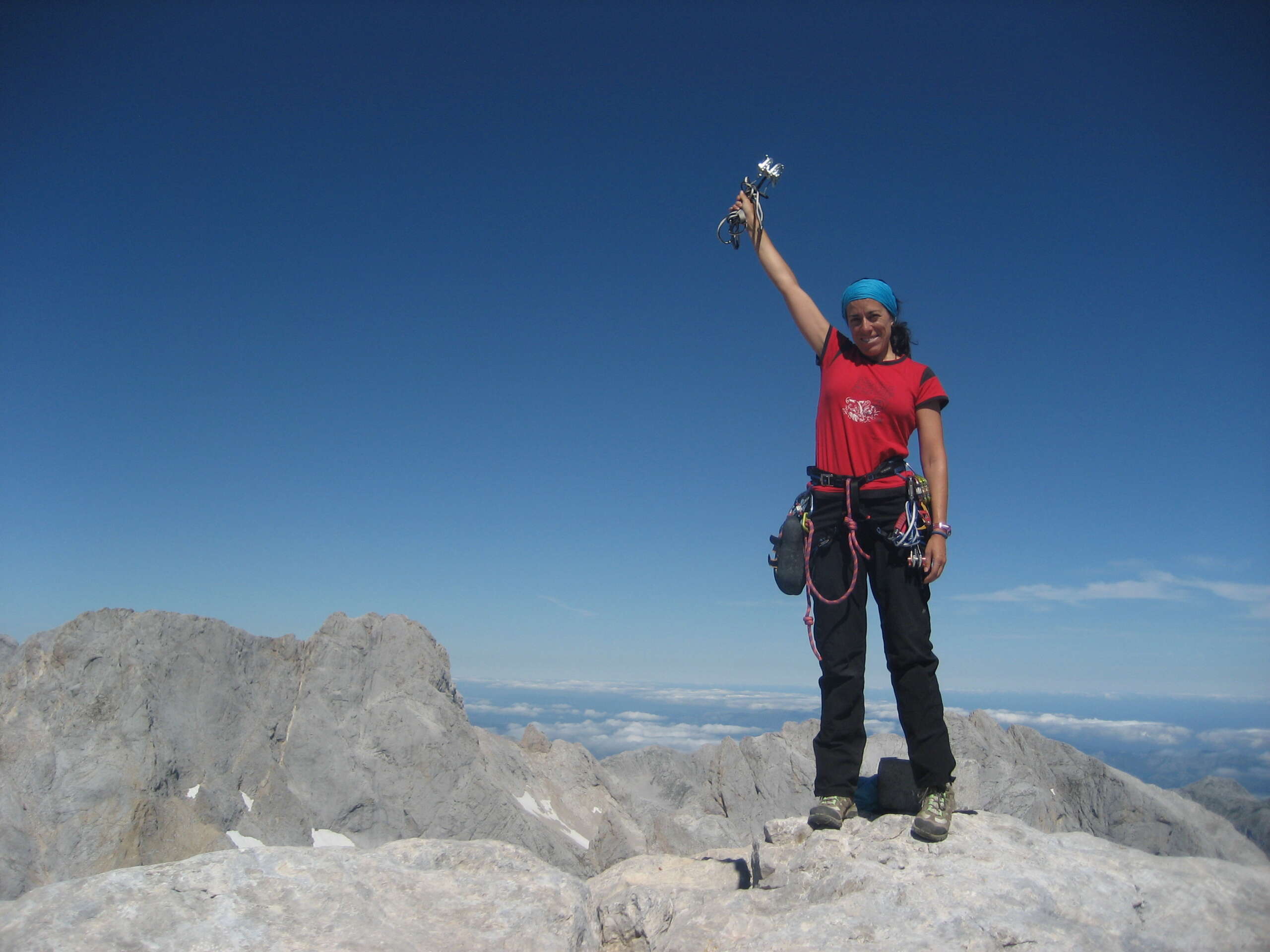 Descripción de la foto de portada: Lara está en la parte derecha de la foto en la cumbre del Picu Urriellu, de pie, muy sonriente y con un brazo en alto con un friend en la mano. Viste ropa deportiva y un arnés de escalada. Detrás otras cumbres y un mar de nubes.