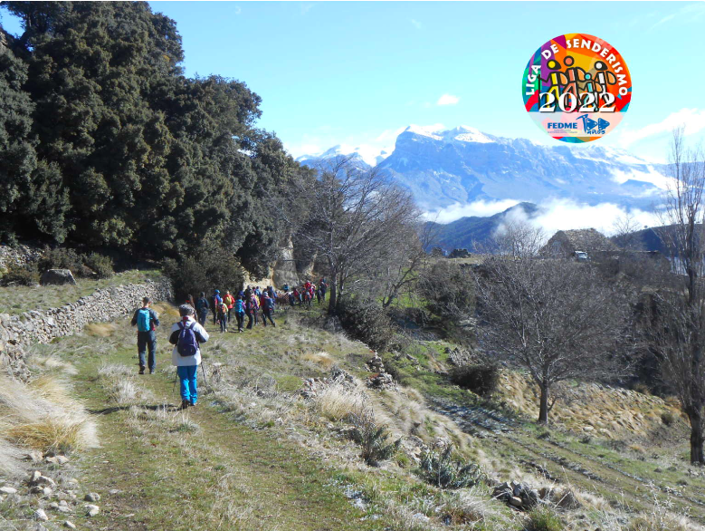 Fotografía de portada: Fotografía en color en la que se presenta un grupo de senderistas caminando por los bancales cercanos a los restos de un pueblo abandonado. En el fondo, Peña Montañesa y las sierra colindantes, con las cumbres nevadas, mientras que las zonas bajas del valle permanecen las nieblas. En el extremo superior derecha aparece el logo de la Liga de Senderismo FEDME 2022.