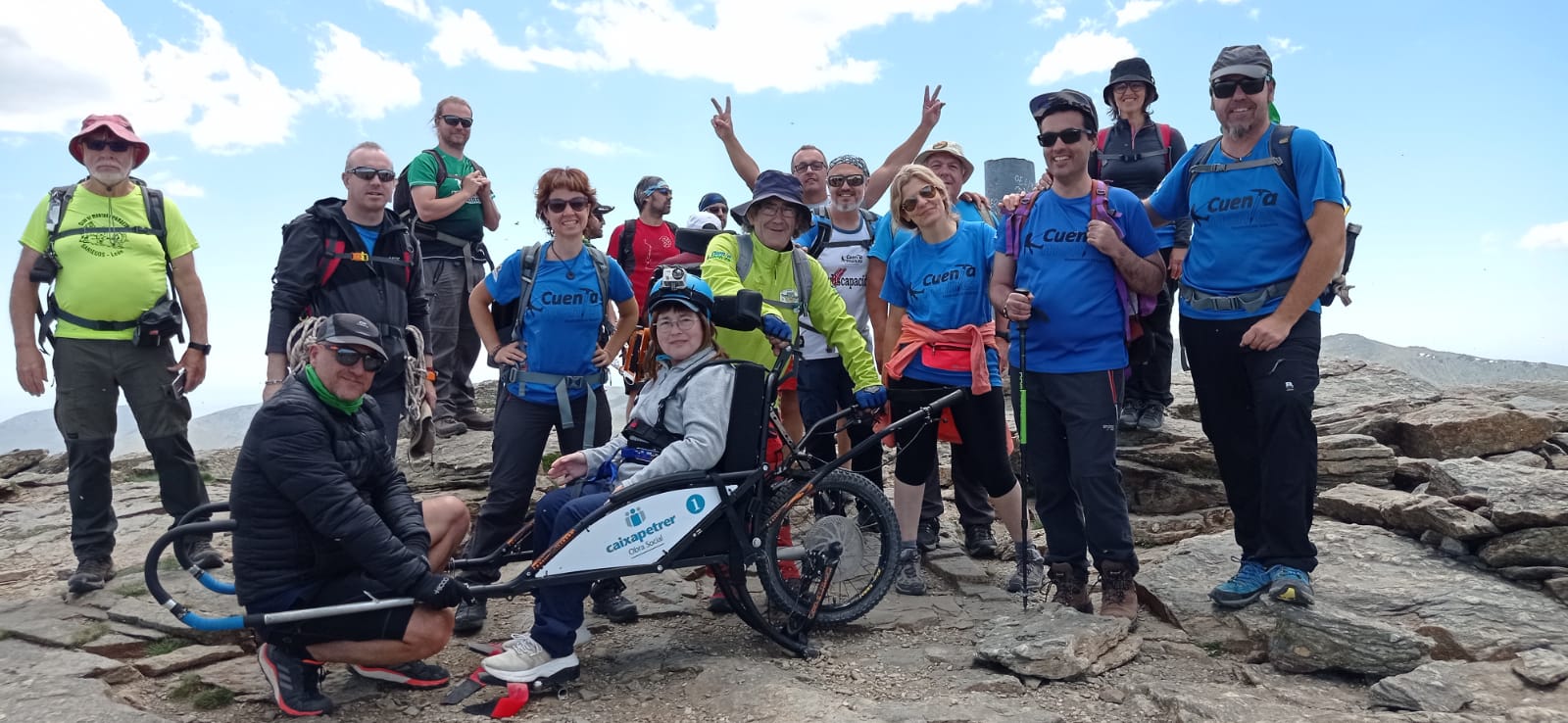 -“Cima Peñalara Cuentamontes”: La foto muestra a un grupo de voluntarios de Cuentamontes (Sección de Montañismo Inclusivo y Adaptado del “Centro Excursionista Petrer”) en la cima de Peñalara (sierra de Guadarrama). Entre ellos, una usuaria de silla Joelëtte.