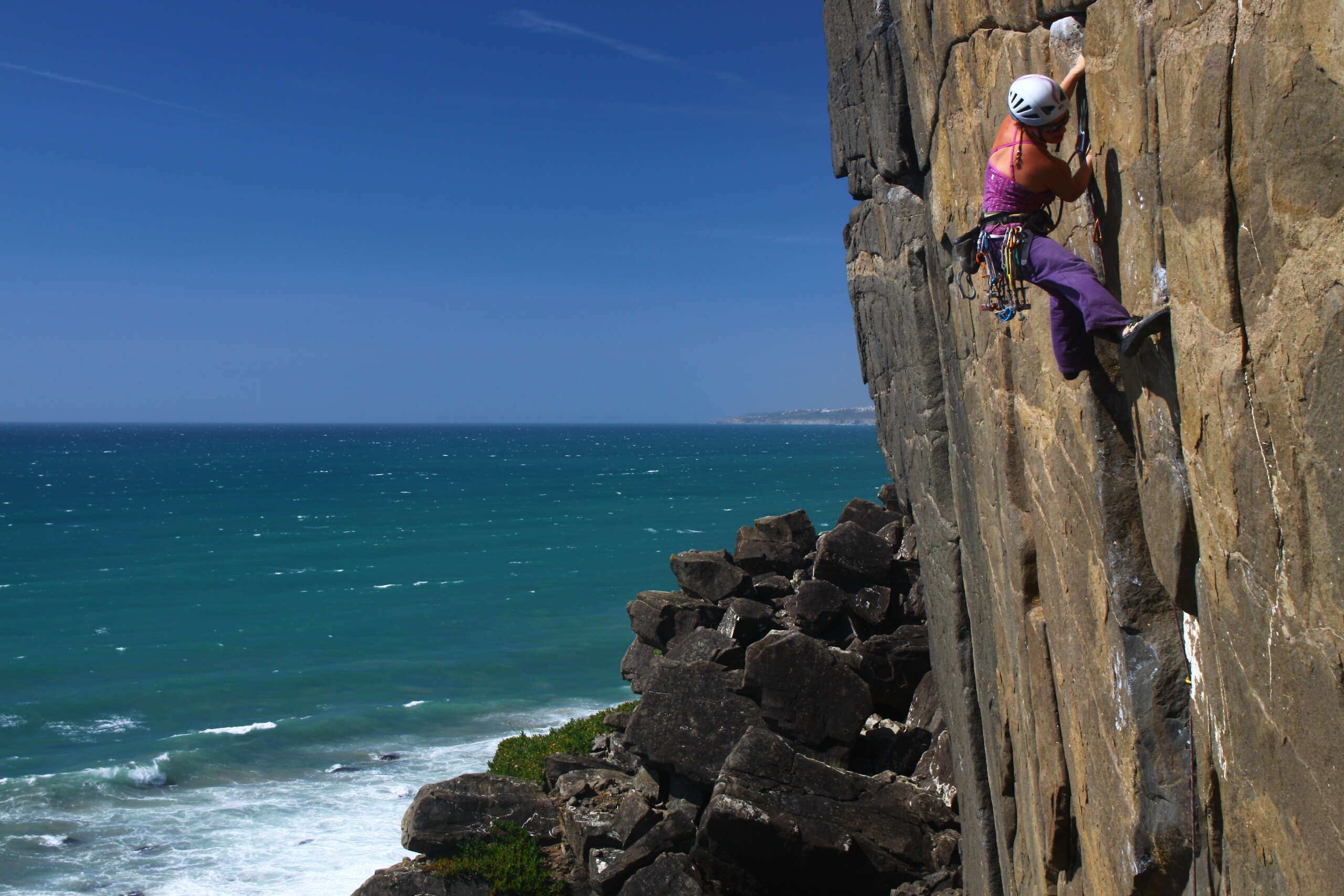 Inma Garrido aparece a la derecha de la foto escalando en una pared vertical. Al pie de vía se ven rocas y el mar que también ocupa toda la parte izquierda de la foto. Está tomada en Portugal en Casal de Pianos y el crédito de la foto es de Iván Jara