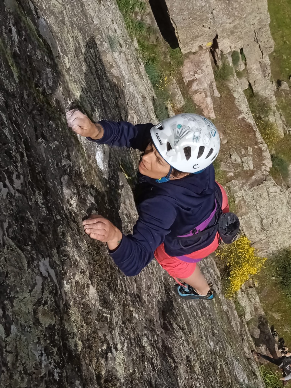 Almudena García aparece en primer plano escalando, con un casco blanco y una camiseta de manga larga azul, en la escuela de escalada que está en el El Castellar, junto a su casa, en su cara se refleja el esfuerzo y el disfrute al mismo tiempo, al fondo un patio espectacular de varios metros.