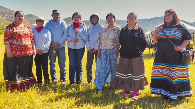 Grupo de mujeres en campo de hierba, alguna de ellas con vestimenta típica indígena kumiay
