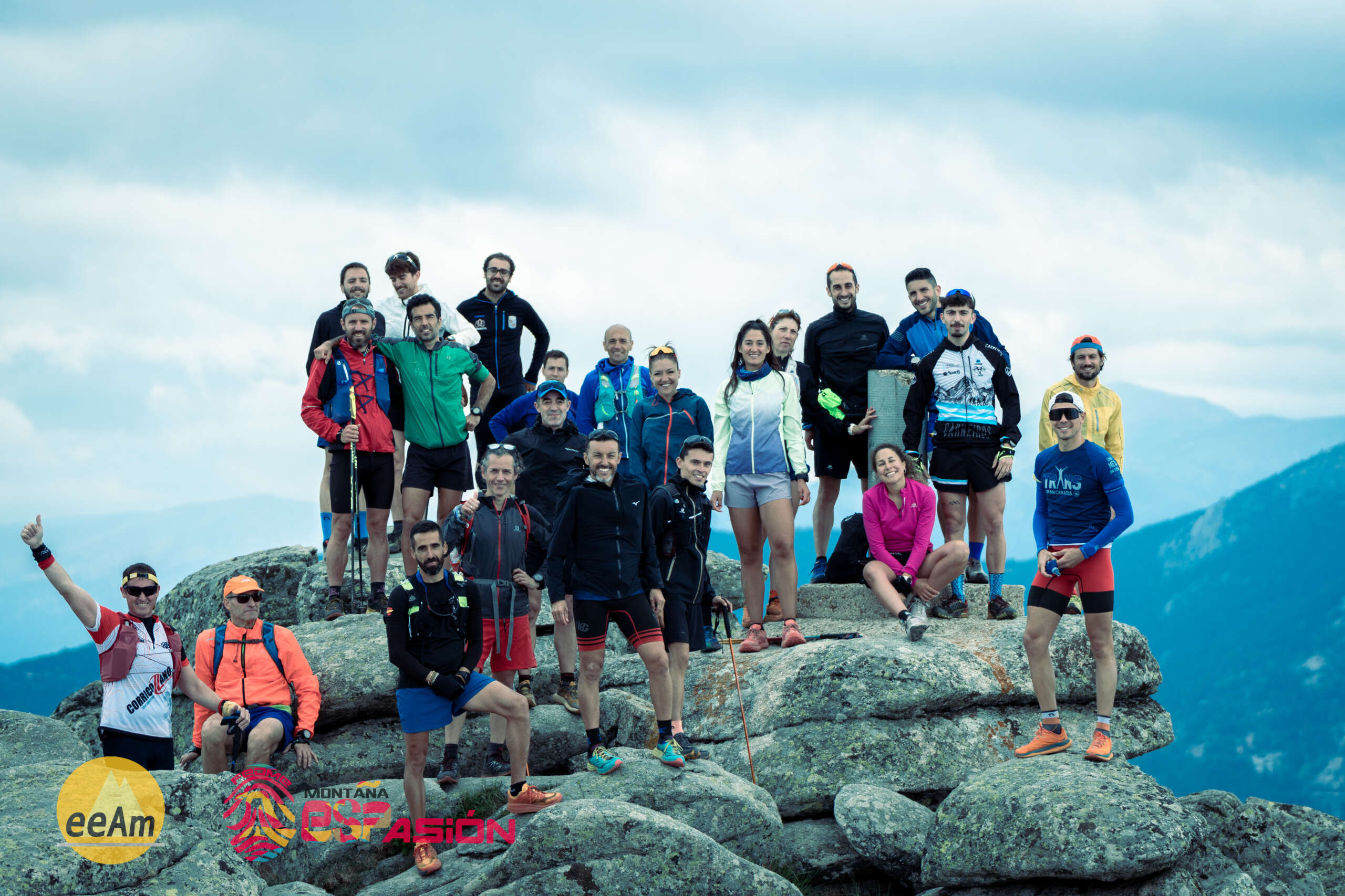 en la foto aparece un grupo de 22 personas, todas ellas vestidas con equipación de corredores/as por montaña, colocados de pie mirando a la cámara. El grupo está situado en un entorno natural, en la cima de la Peñota (Cercedilla) sobre una superficie de rocas.