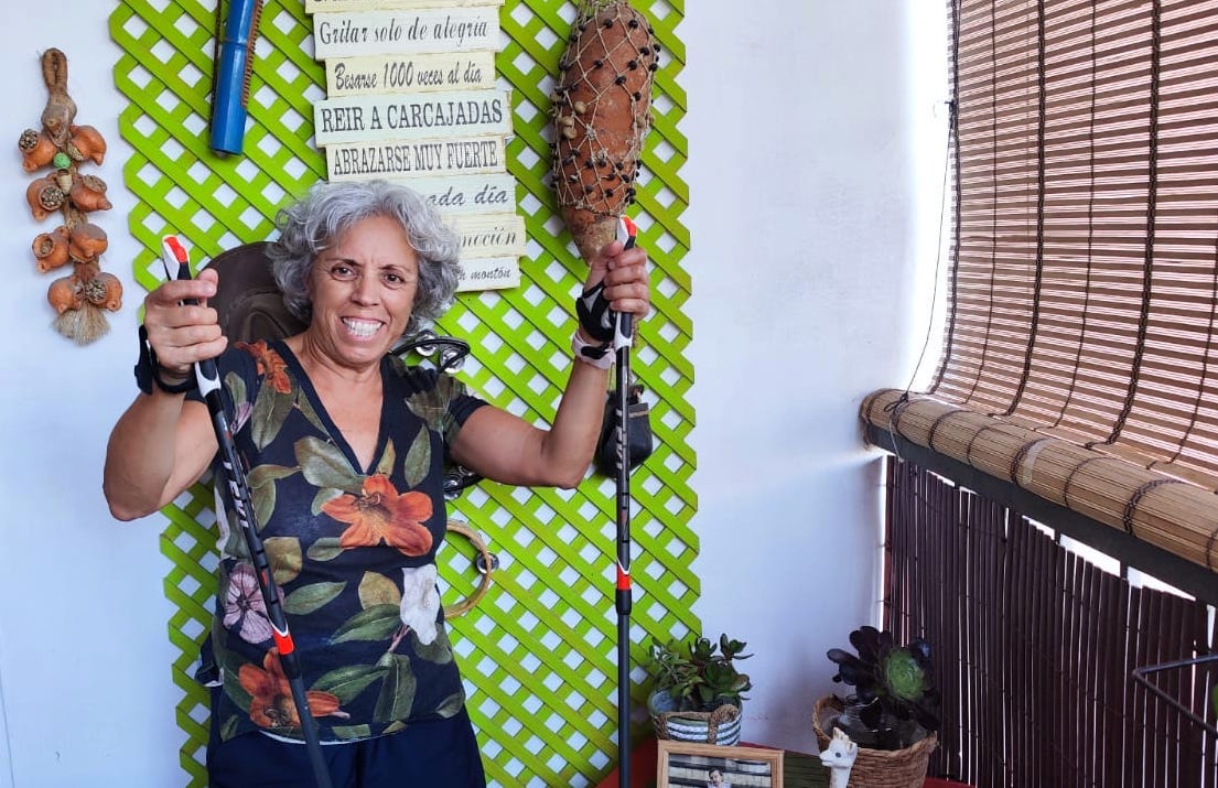 Carmen aparece muy sonriente mostrando en alto los bastones de marcha nórdica. La foto está tomada de cintura para arriba, en casa.