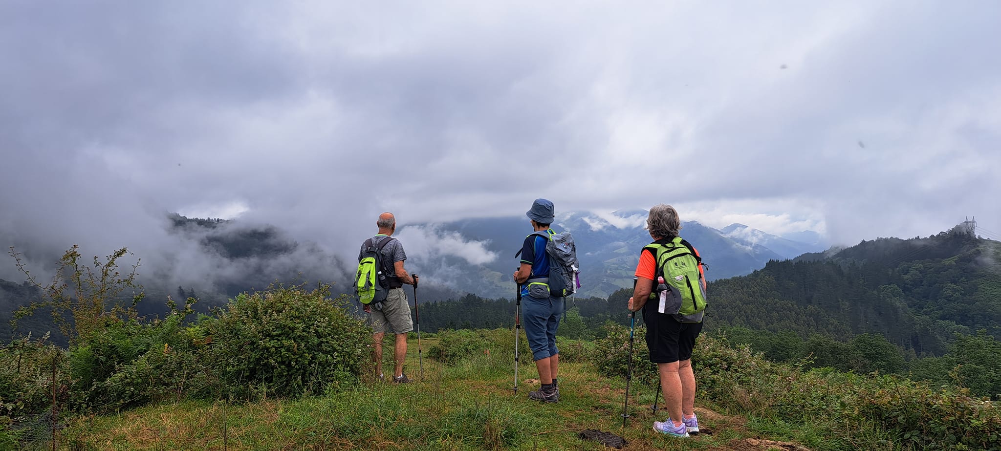 Imagen en color que muestra a un tres senderistas, contemplando un paisaje con nieblas bajas