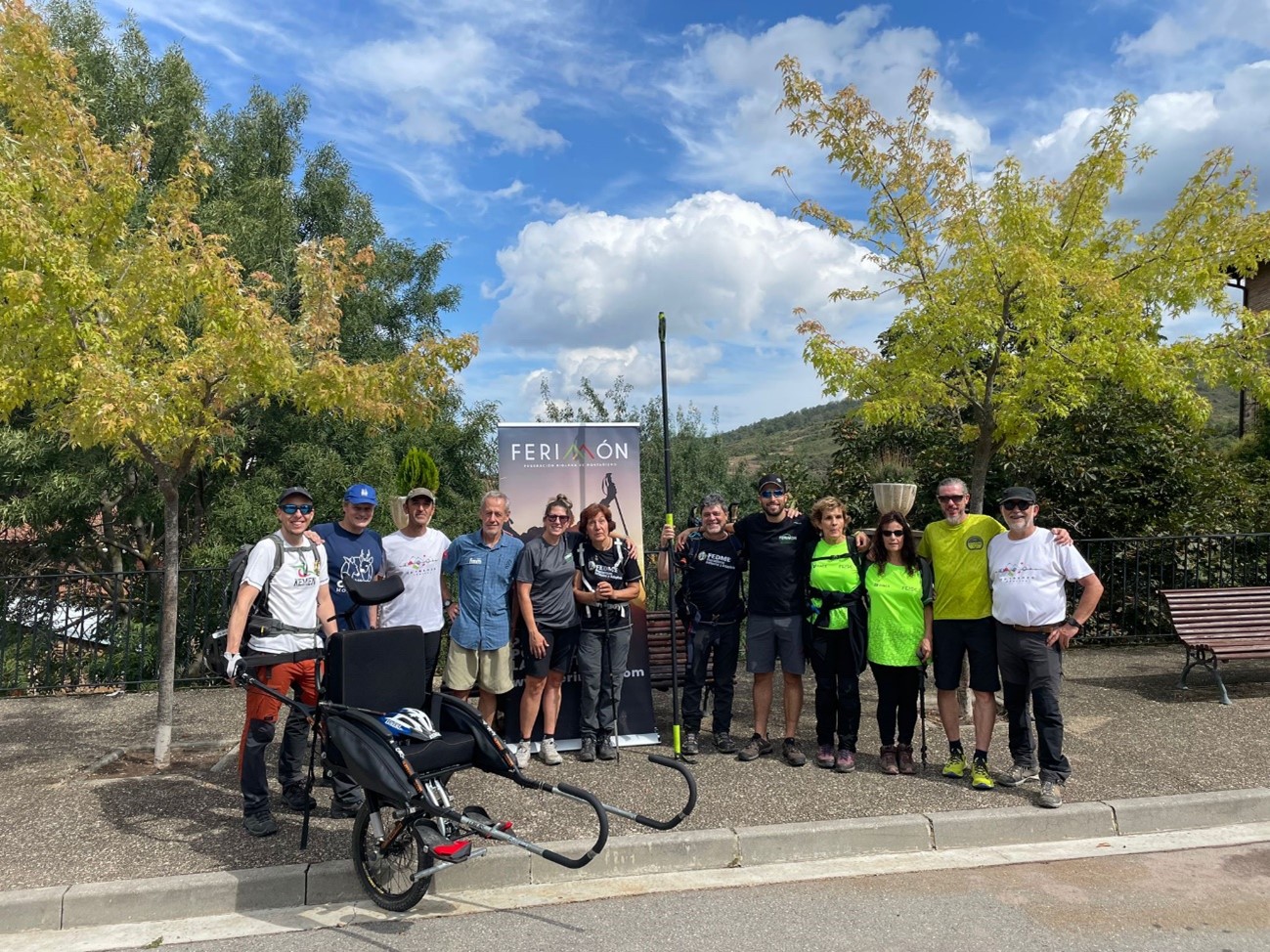 Foto de grupo con un cartel de la Federación de Montaña de La Rioja (FERIMON). Está hecha en el pueblo de Ajamil de Cameros, y en ella posan los asistentes al Encuentro (representantes de clubes y federaciones de varios puntos de España) y los organizadores (FEDME y FERIMON).