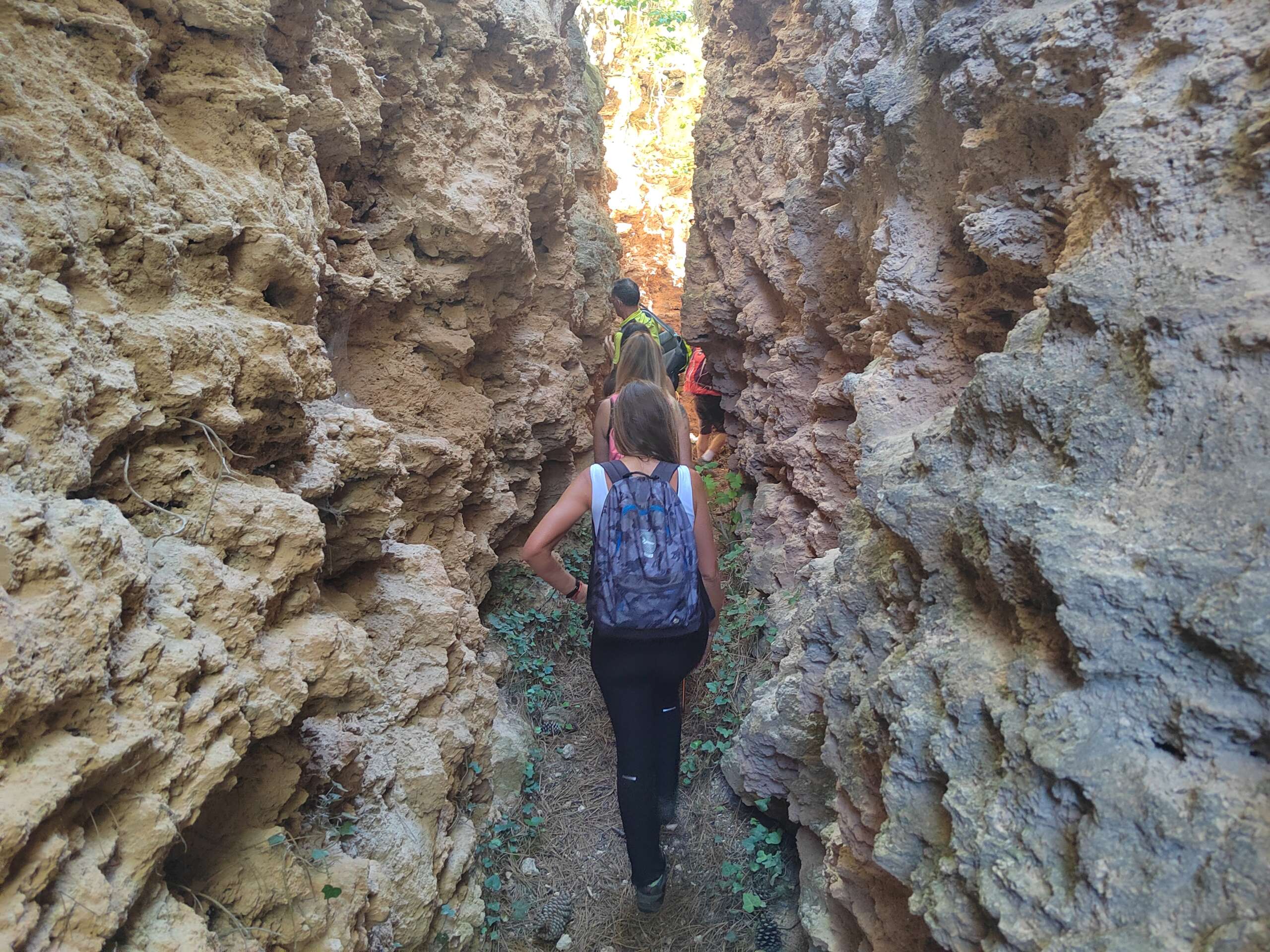 Fotografía en color que presenta a una serie de senderistas caminando en un estrecho desfiladero de roca