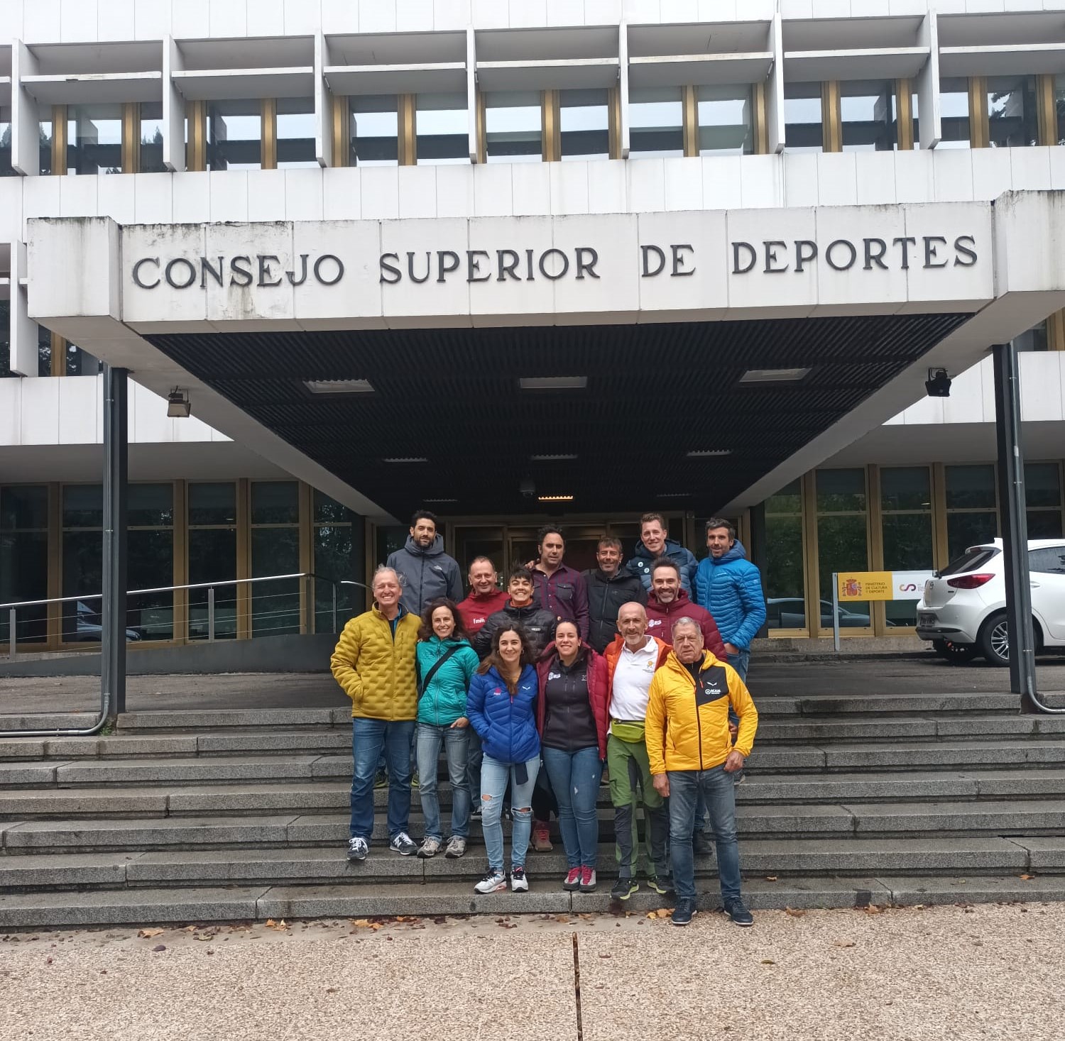 de izquierda a derecha, en la mitad izquierda del cartel aparece una foto de una sala de reuniones donde se puede apreciar, en primer plano, un ordenador portátil, una botella de agua y un taco de folios blancos donde está escrito “Encuentro de Escuelas”. En la mitad derecha, en la esquina superior derecha del cartel, está colocado un trapecio rectángulo de color naranja sobre el que está escrito en negro y mayúsculas “ENCUENTRO ESCUELAS AUTONÓMICAS 2023”. Bajo esto, en la parte inferior derecha del cartel, sobre un fondo blanco se encuentran los logos de la EEAM (las siglas de EEAM subrayadas con una línea gris claro sobre un círculo amarillo con el perfil de unas montañas en color amarillo más claro en su interior) y de la FEDME (una huella dactilar de colores rojo, amarillo y azul cuyas líneas forman el Torreón de los Galayos con un pájaro sobrevolándolo. A la derecha de la huella aparecen las letras Montaña en negro, debajo ESP en colores rojo y amarillo y debajo las letras Federación Española de Deportes de Montaña y Escalada en negro).