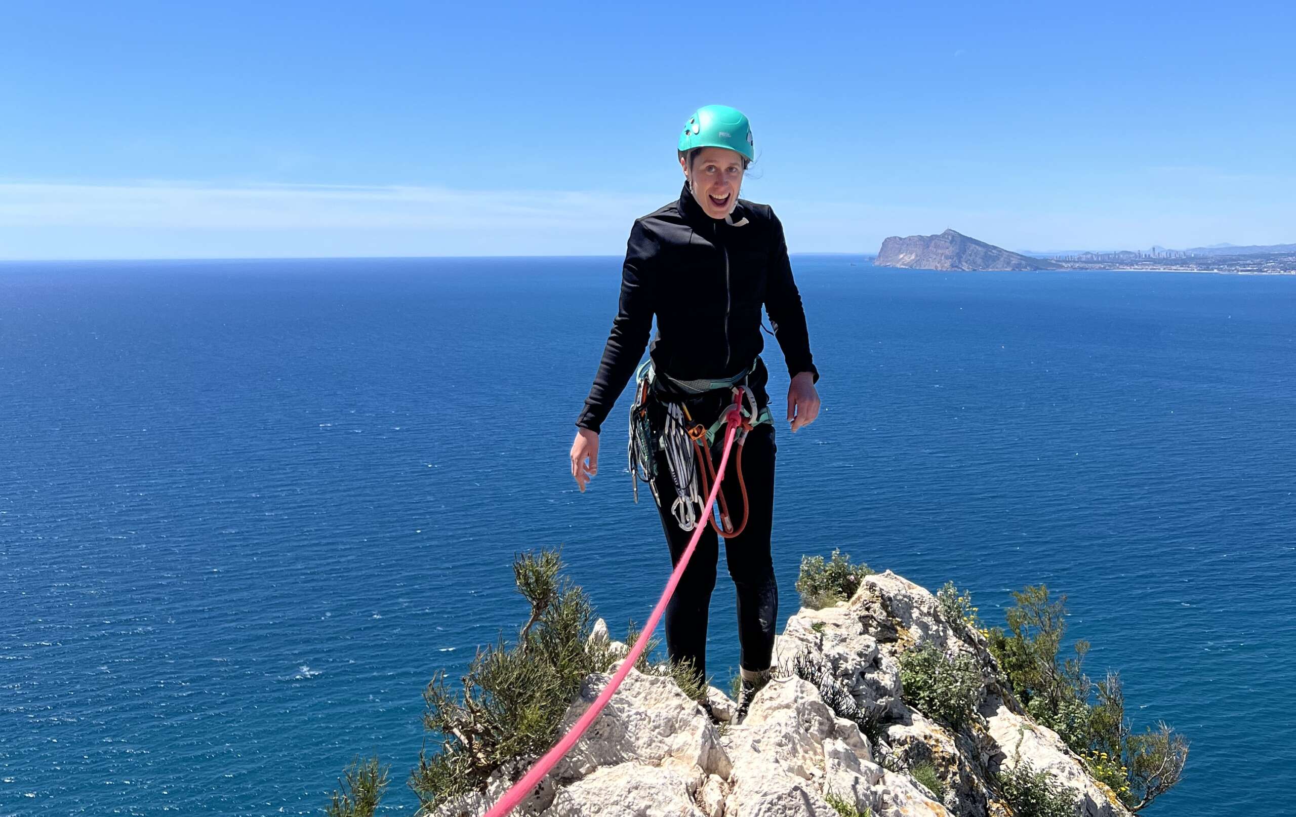 Descripción de la foto: Beatriz aparece de pie con expresión de felicidad en la cima del Peñón de Ifach (Alicante). Está encordada y equipada con arnés, casco y diverso material de escalada. Al fondo el mar y el horizonte.