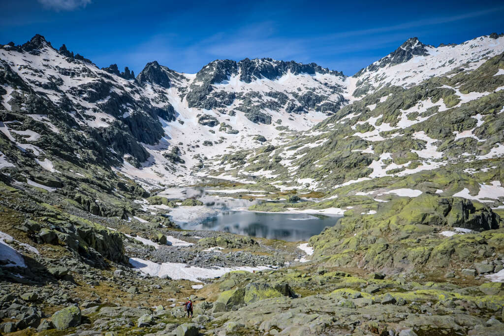 El Circo de Gredos en primavera, con un cielo azul intenso y nieve aún en las laderas, con visualización de derecha a izquierda del Almanzor, Cuchillar de las Navajas, Peñón del Casquerazo, Los Tres Hermanitos, Risco de la Ventana, La Campana y el Morezón, en el centro la Laguna Grande de Gredos y al comienzo de esta el Refugio Laguna Grande de Gredos. Autor de la foto Chema Mancebo.
