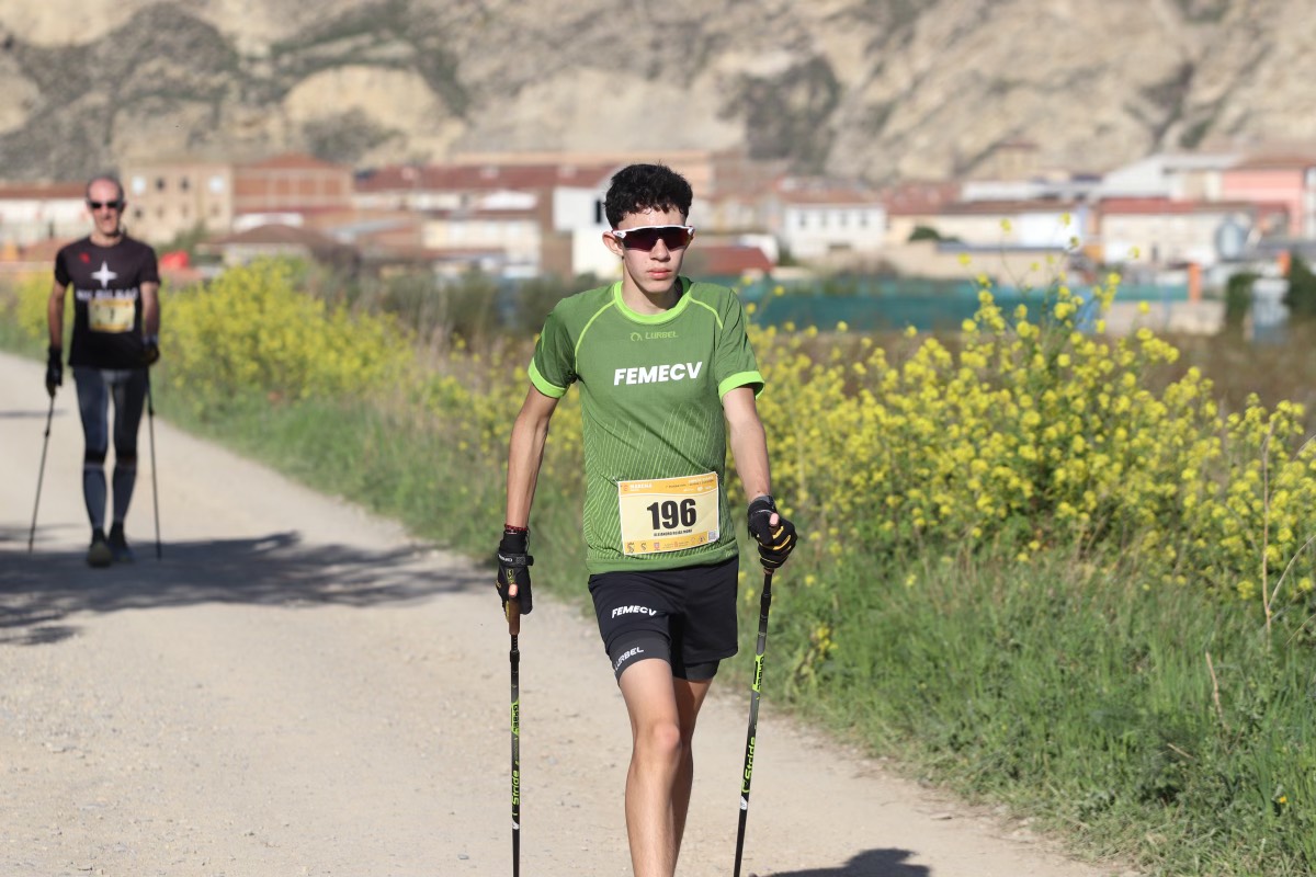 Descripción foto para personas con discapacidad visual:  Alejandro aparece en el centro de la foto practicando marcha nórdica en una pista vistiendo la una camiseta y pantalón corto de la selección de la comunidad valenciana con el dorsal 196. Lleva gafas de sol y es la primera prueba de Copa de España celebrada en Azagra este 2024. Detrás se ve a otro competidor en la lejanía.