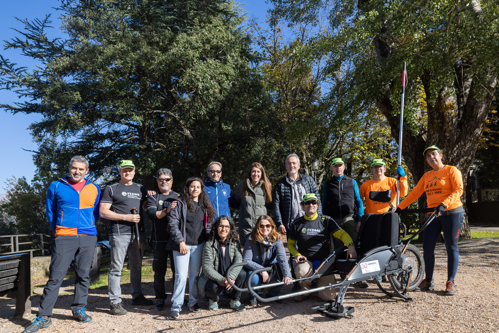 Foto 2: fotografía de grupo realizada en el exterior. 13 personas componen el grupo fotografíado. Todas ellas mirando de frente junto a una silla joelette utilizada en la jornada del domingo.