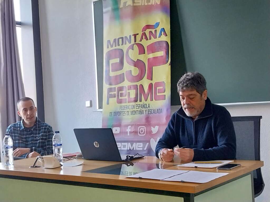 Foto 2: La fotografía muestra a rancis Bueno, Responsable del Comité de Montañismo Inclusivo y Adaptado en el interior de un aula de la Facultad de Ciencias de la Actividad Física y del Deporte. Francis está sentado exponiendo una explicación desde la mesa del aula. A su derecha se encuentra sentado el segundo ponente.