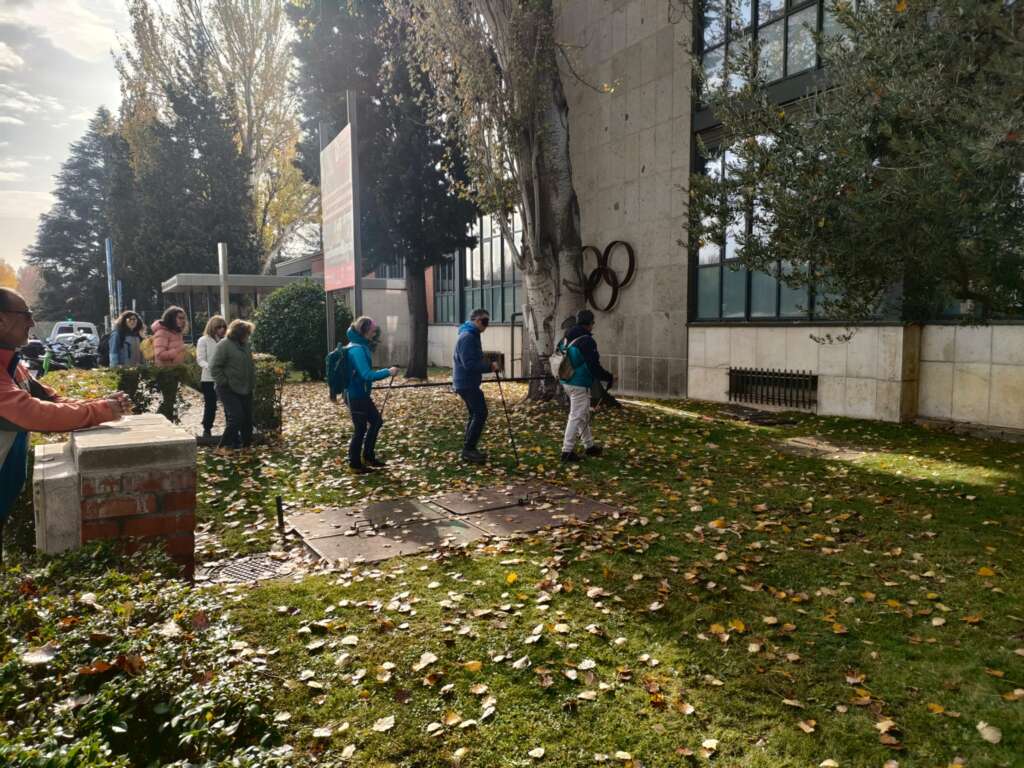 Foto 3: Un grupo de personas realiza una sesión práctica en el exterior de la Facultad de Ciencias de la Actividad Física y del Deporte. Una sesión en la que practican el guiado de personas ciegas, con los ojos tapados y el uso de bastones.