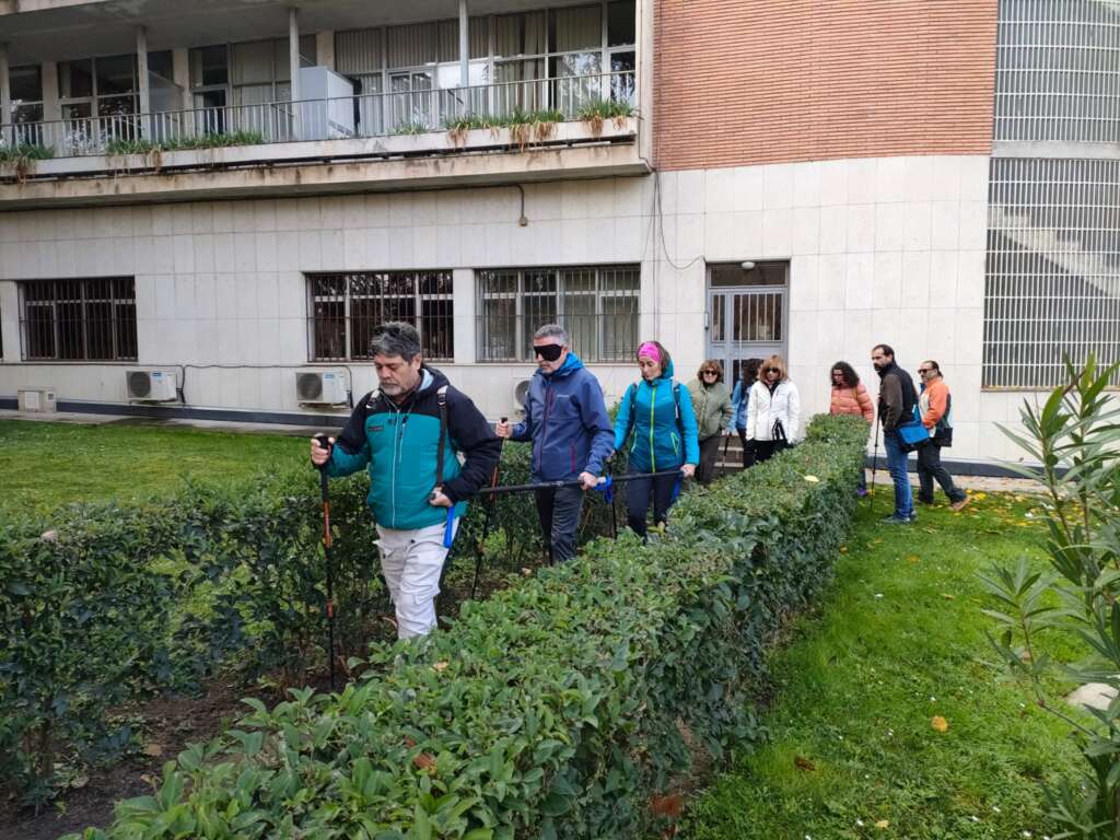 Foto 5: Un grupo de personas hacen una práctica para conocer el uso de la barra direccional. Uno de los participantes, un hombre situado en el centro de la barra direccional, lleva tapados los ojos para conocer